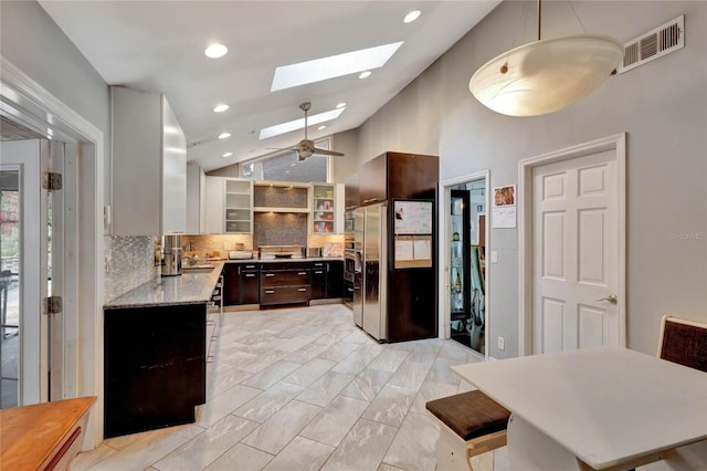 kitchen with dark brown cabinetry, a skylight, tasteful backsplash, high vaulted ceiling, and stainless steel fridge