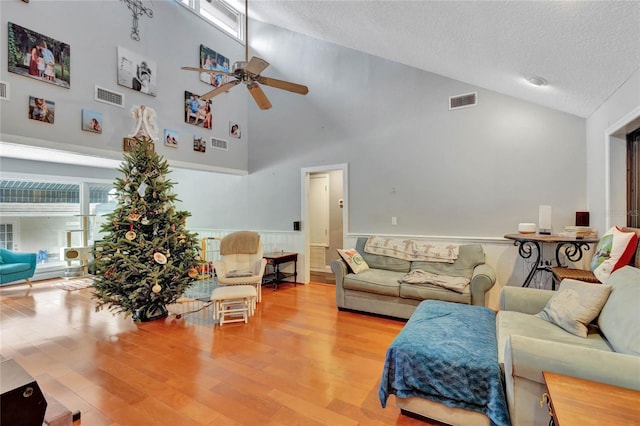 living room with ceiling fan, high vaulted ceiling, a textured ceiling, and light wood-type flooring