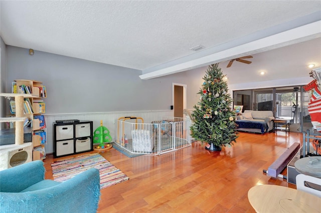 living room with ceiling fan, beamed ceiling, wood-type flooring, and a textured ceiling