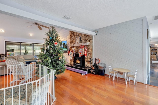 living room featuring a textured ceiling, ceiling fan, beam ceiling, hardwood / wood-style floors, and a wood stove