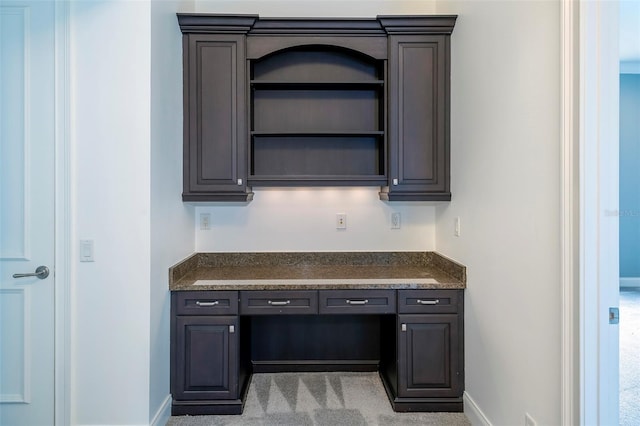 interior space with dark brown cabinetry, built in desk, and light colored carpet