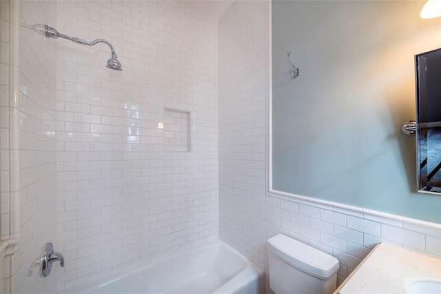 full bathroom featuring tiled shower / bath, vanity, toilet, and tile walls