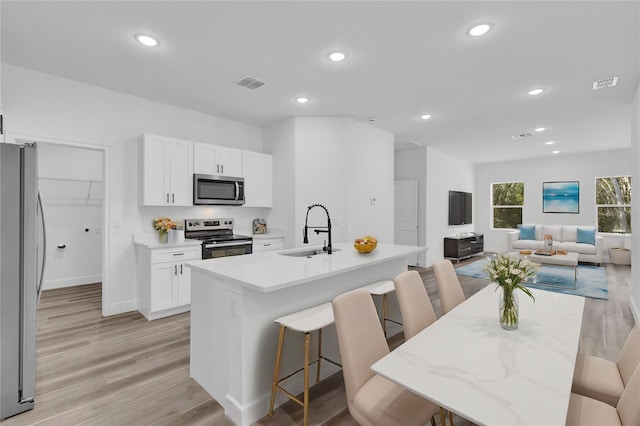 kitchen with stainless steel appliances, a kitchen island with sink, a breakfast bar area, white cabinetry, and sink