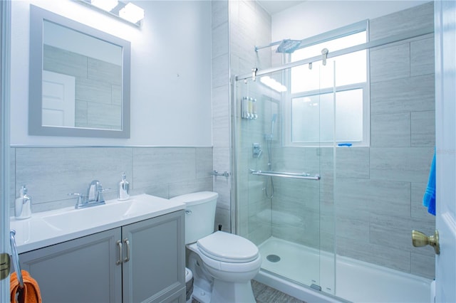 bathroom with vanity, a shower with door, toilet, and tile walls