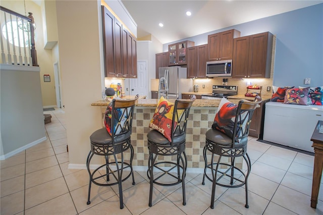 kitchen with light stone countertops, appliances with stainless steel finishes, a kitchen bar, vaulted ceiling, and light tile patterned floors