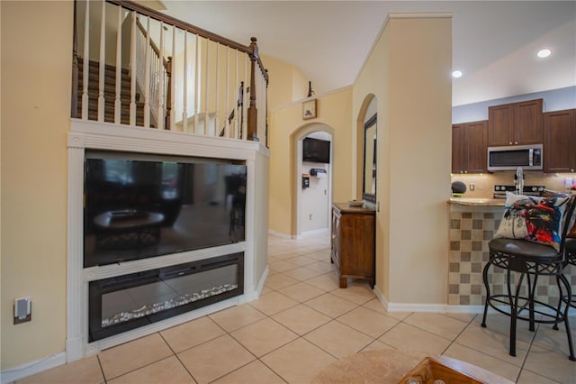 kitchen featuring decorative backsplash, light tile patterned floors, a kitchen bar, and vaulted ceiling