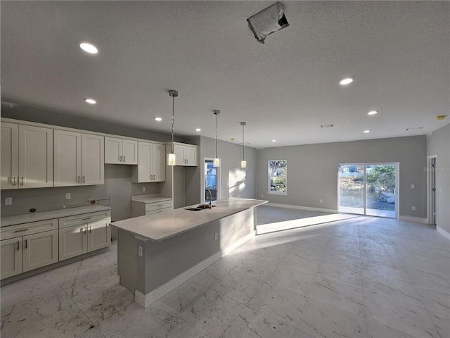 kitchen with sink, an island with sink, a textured ceiling, and white cabinetry