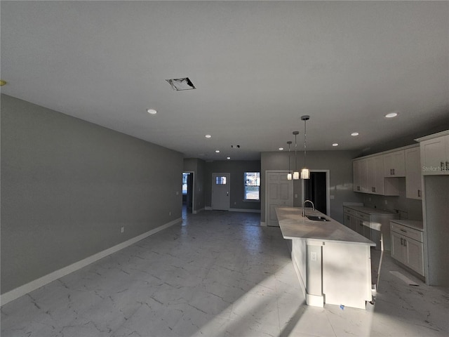 kitchen with a center island with sink, hanging light fixtures, a breakfast bar, sink, and white cabinetry