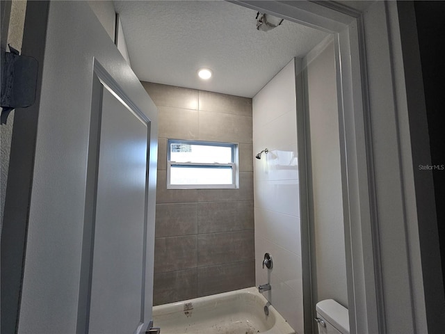 bathroom with a textured ceiling, toilet, and tiled shower / bath