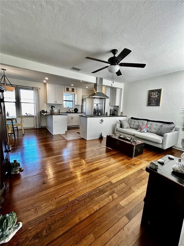 living room featuring a textured ceiling, wood finished floors, visible vents, and a ceiling fan