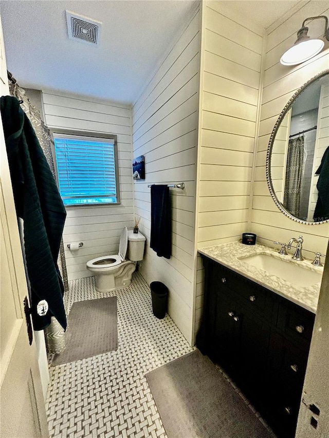 full bathroom with toilet, wood walls, visible vents, and vanity