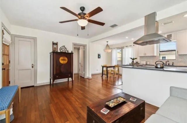 living area with dark wood-type flooring, visible vents, baseboards, and a ceiling fan