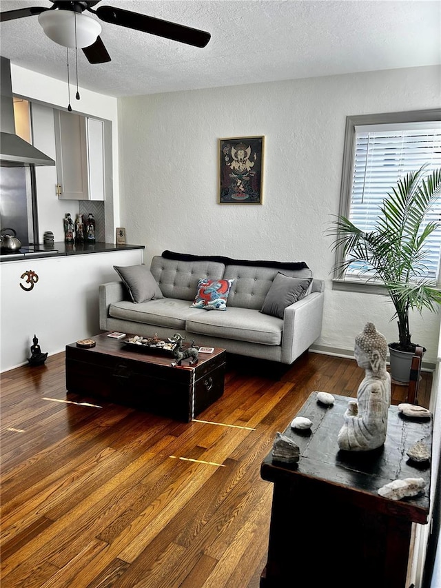 living room with dark wood-type flooring, a textured wall, a textured ceiling, and ceiling fan