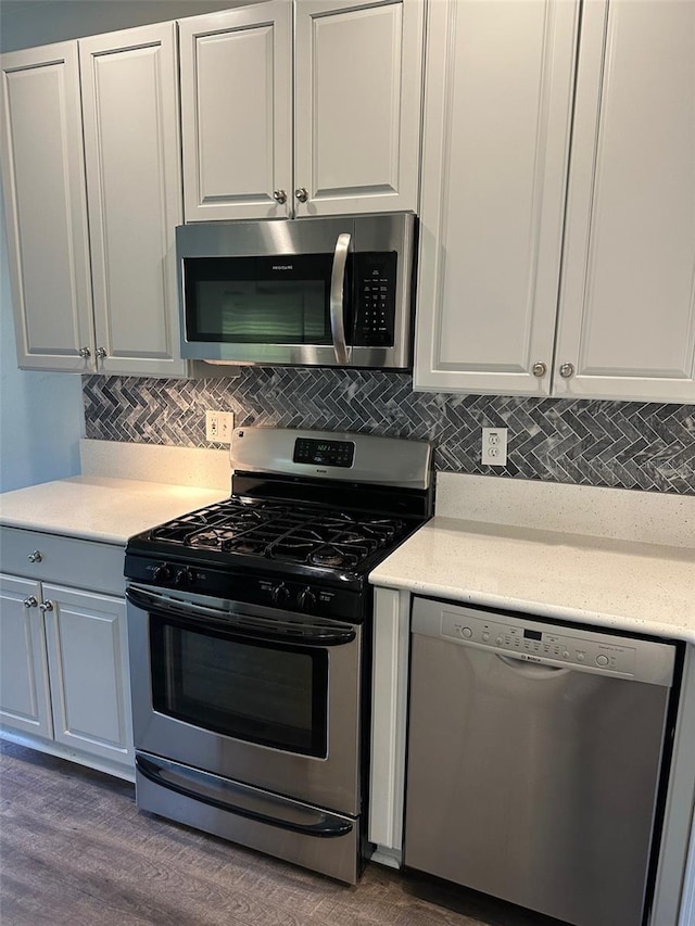 kitchen with backsplash, white cabinetry, stainless steel appliances, and hardwood / wood-style flooring