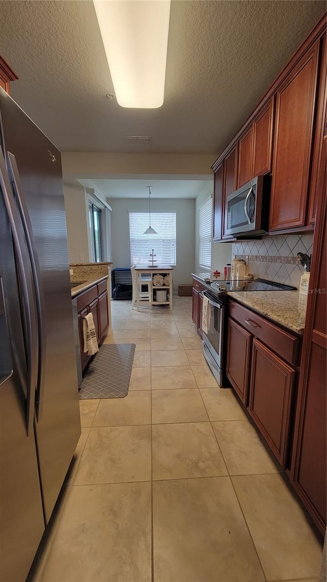 kitchen with tasteful backsplash, a textured ceiling, stainless steel appliances, light tile patterned floors, and hanging light fixtures