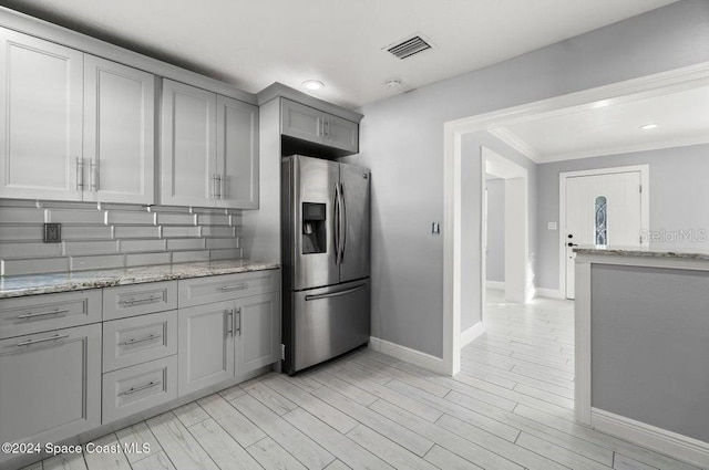 kitchen with light stone countertops, stainless steel fridge with ice dispenser, light wood-type flooring, and tasteful backsplash