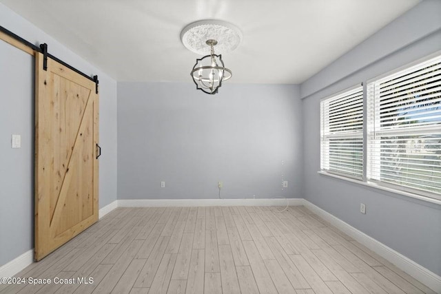 unfurnished room featuring a barn door, an inviting chandelier, and light hardwood / wood-style flooring