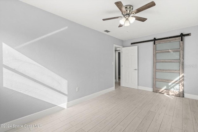 unfurnished bedroom featuring a barn door, ceiling fan, and light hardwood / wood-style flooring