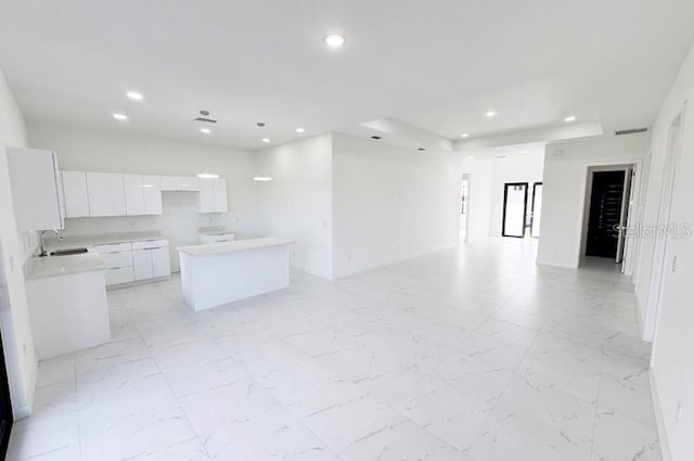 kitchen featuring a tray ceiling, a center island, white cabinets, and sink