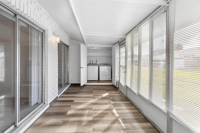 corridor with washer and dryer, wood-type flooring, and brick wall