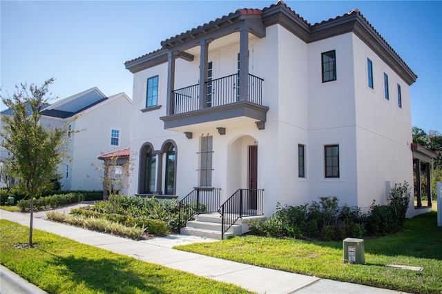 mediterranean / spanish house featuring a balcony and a front lawn