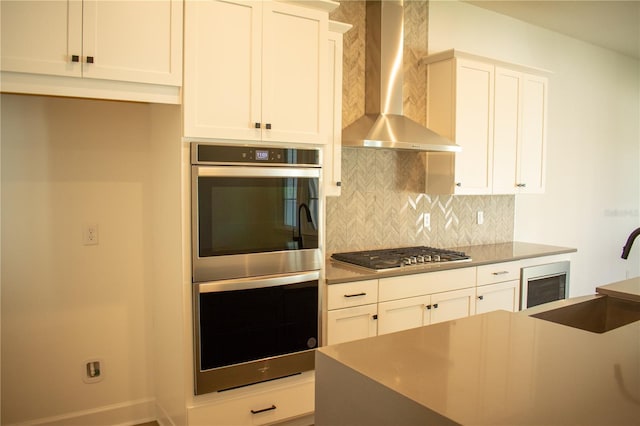 kitchen featuring wall chimney exhaust hood, decorative backsplash, white cabinetry, and appliances with stainless steel finishes