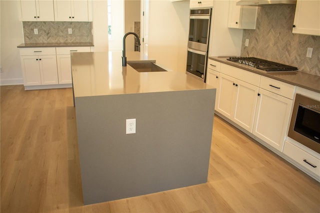 kitchen featuring sink, stainless steel appliances, a center island with sink, and light wood-type flooring