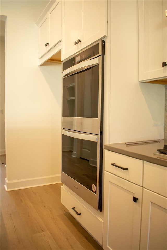 kitchen featuring white cabinets, light wood-type flooring, and stainless steel double oven