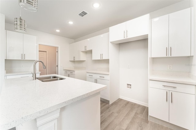 kitchen with sink, white cabinets, hanging light fixtures, and light wood-type flooring