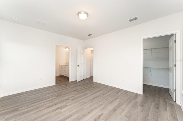 unfurnished bedroom featuring a closet, a walk in closet, light hardwood / wood-style flooring, and ensuite bath