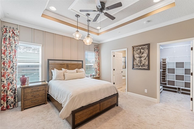 carpeted bedroom featuring a walk in closet, ensuite bath, ornamental molding, a raised ceiling, and ceiling fan