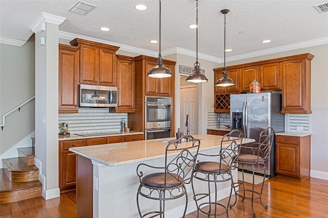 kitchen featuring backsplash, a center island with sink, hanging light fixtures, sink, and appliances with stainless steel finishes