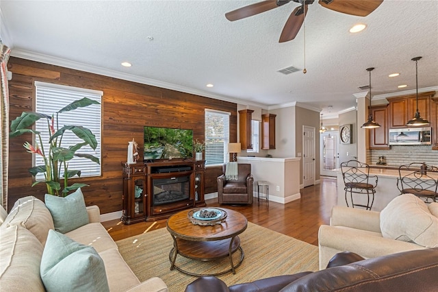 living room with dark wood-type flooring, ceiling fan, ornamental molding, a textured ceiling, and a fireplace