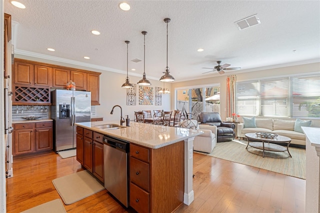 kitchen featuring sink, stainless steel appliances, crown molding, an island with sink, and pendant lighting