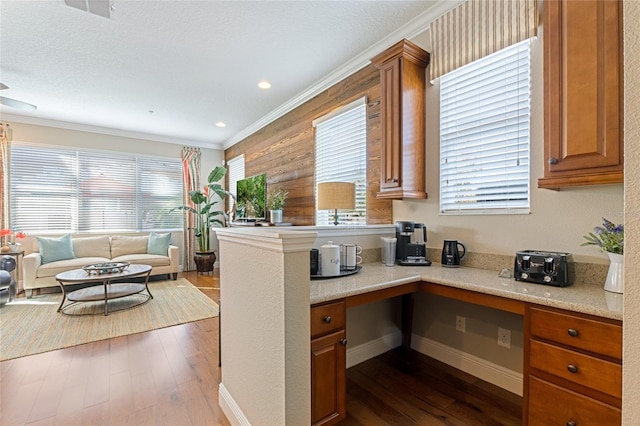 kitchen with a wealth of natural light, dark hardwood / wood-style flooring, built in desk, and ornamental molding