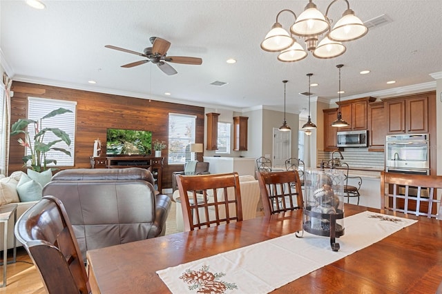 dining area featuring a textured ceiling, ceiling fan with notable chandelier, crown molding, and wooden walls