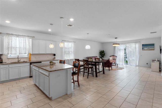 kitchen with tasteful backsplash, pendant lighting, a kitchen island, sink, and light stone counters