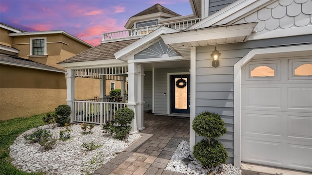 exterior entry at dusk featuring a balcony and a garage