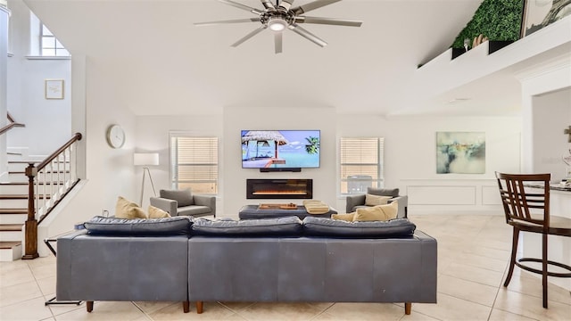 2377 Victoria Dr, Davenport, FL 33837 - living area with light tile patterned floors, a ceiling fan, a glass covered fireplace, stairway, and high vaulted ceiling