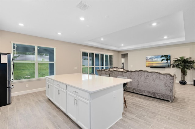 kitchen with white cabinets, stainless steel fridge, light wood-type flooring, and a kitchen island