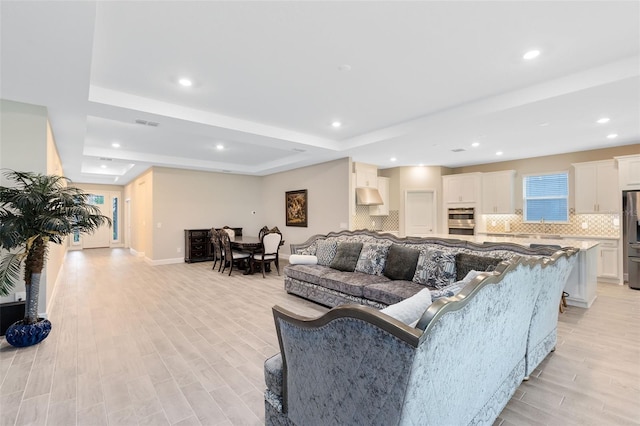 living room featuring a raised ceiling and light hardwood / wood-style floors