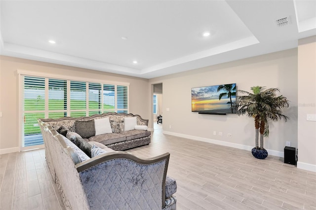 living room with light hardwood / wood-style floors and a raised ceiling