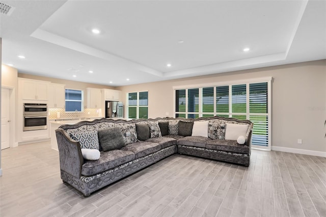 living room with light hardwood / wood-style floors and a tray ceiling