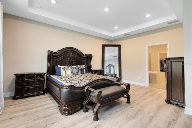 bedroom with a raised ceiling, light wood-type flooring, and ensuite bath