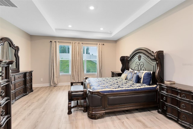 bedroom with light wood-type flooring and a raised ceiling