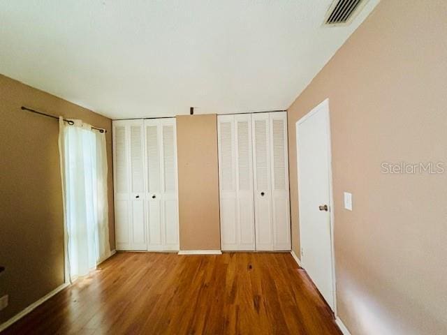 unfurnished bedroom with wood-type flooring and two closets