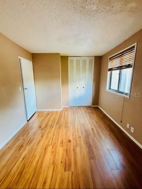 unfurnished bedroom with light wood-type flooring, a textured ceiling, and a closet