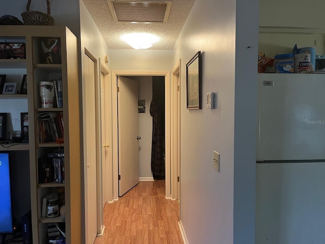 corridor with light wood-type flooring and a textured ceiling