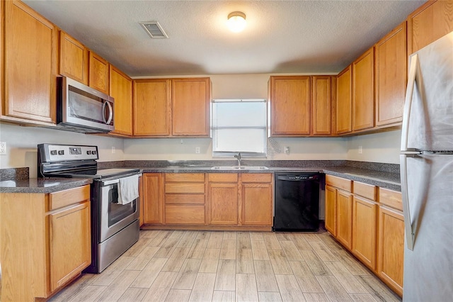 kitchen featuring sink, light hardwood / wood-style flooring, a textured ceiling, and appliances with stainless steel finishes