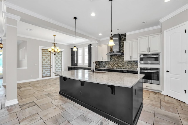 kitchen with sink, wall chimney range hood, crown molding, a kitchen island with sink, and white cabinets